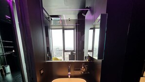 Ein modernes Badezimmer mit einem großem, ovalem Waschbecken, einem Spiegel und Blick auf die Stadt durch große Fenster.