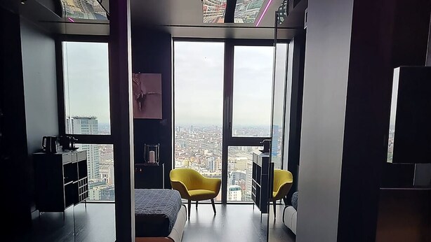 Ein modernes Schlafzimmer mit großem Fenster, einem Bett, einem Schreibtisch und einem Sessel.