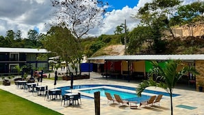 Zona de piscina con sillas de descanso, un área de estar cubierta y un edificio al fondo.