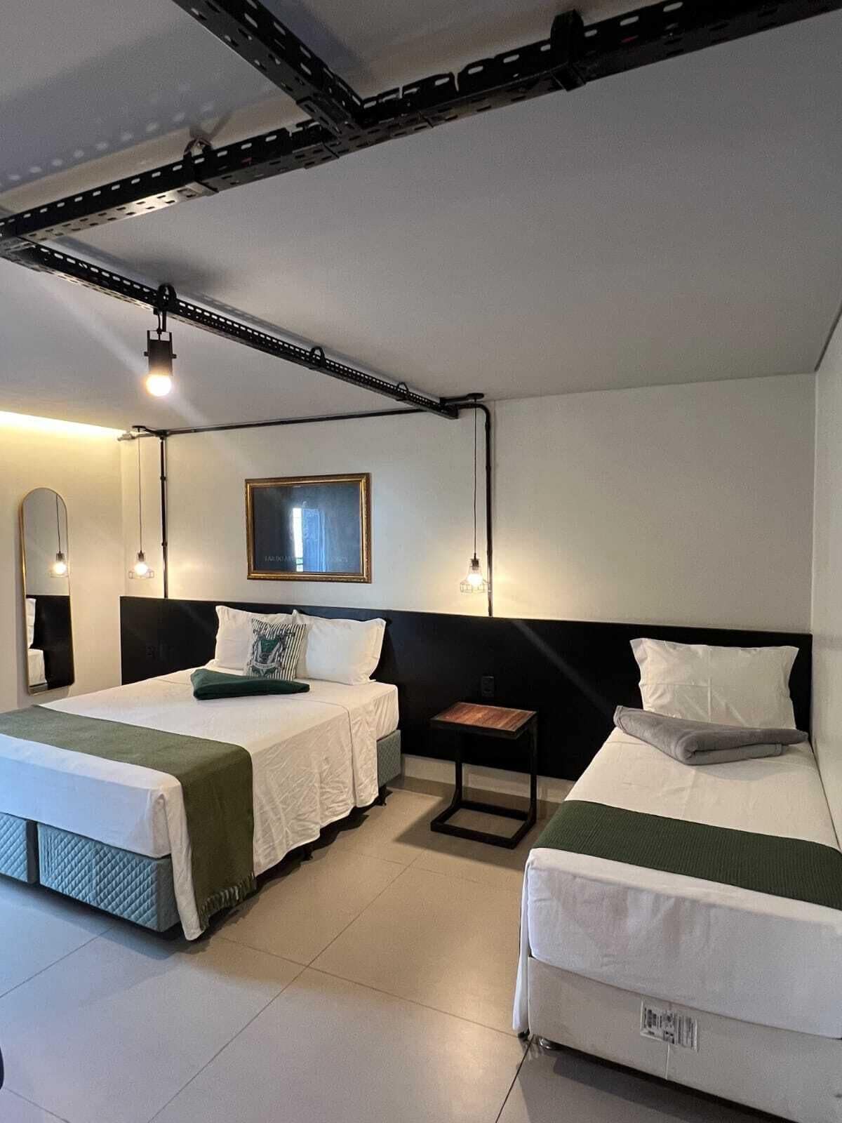 A hotel room with two beds, a small table, a mirror, and a ceiling track system.