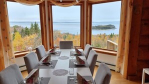 A dining area with a table set for six, large windows offering a view of a lake and forest. - Magical Retreat up to 20 People (St. Peter`s)
