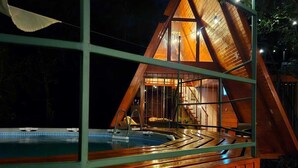 A wooden cabin with a pool, large windows, and a staircase leading to the upper level.