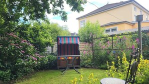 A garden with a wooden bench, a striped table, and a house in the background. - Haus Mira - Wohnung Süden (Wittdün auf Amrum)