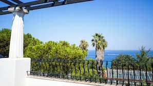 Un balcon agrémenté d’une colonne blanche, d’une balustrade en métal noir et offrant une vue sur l’océan et les palmiers.