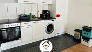 Een moderne keuken met witte kastjes, een roestvrijstalen fornuis, een ingebouwde oven, een wasmachine en een magnetron.