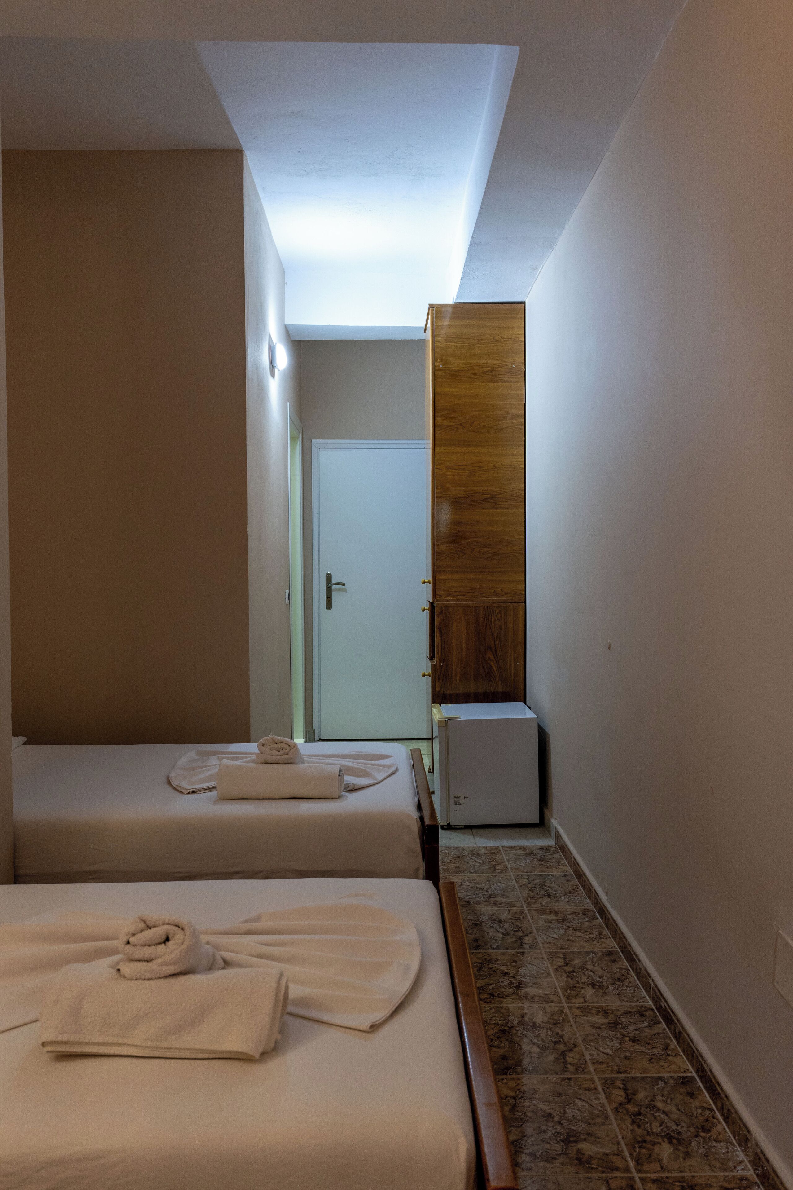Habitación de hotel con dos camas, un armario de madera y un refrigerador pequeño.