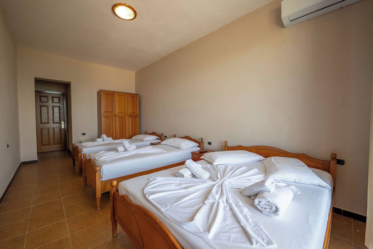 A hotel room with three wooden beds, each with white linens and towels. There is a wooden wardrobe and an air conditioning unit on the wall.