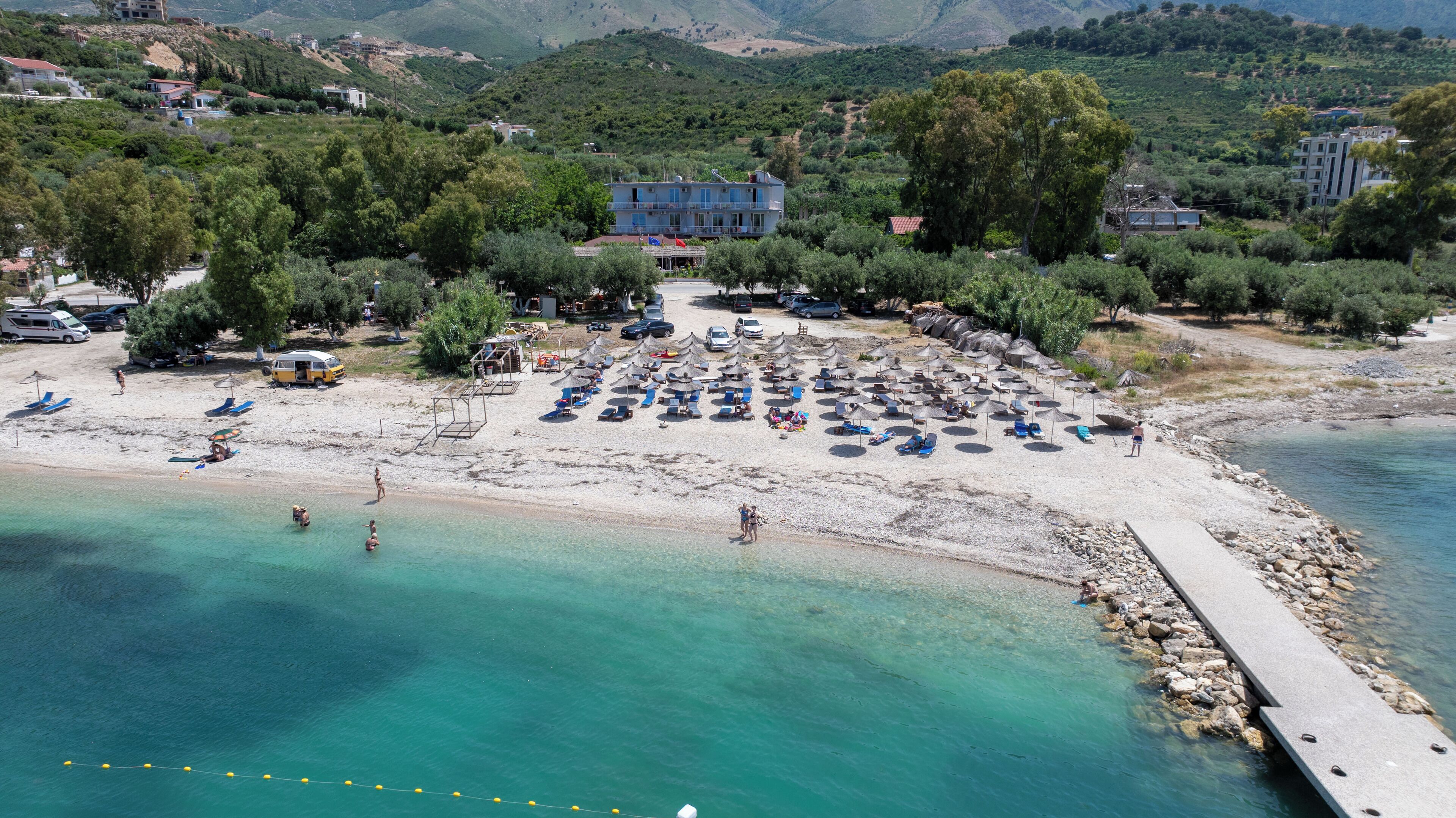Une plage avec de nombreuses chaises longues et des parasols, un bâtiment doté d’un balcon, et une côte rocheuse.