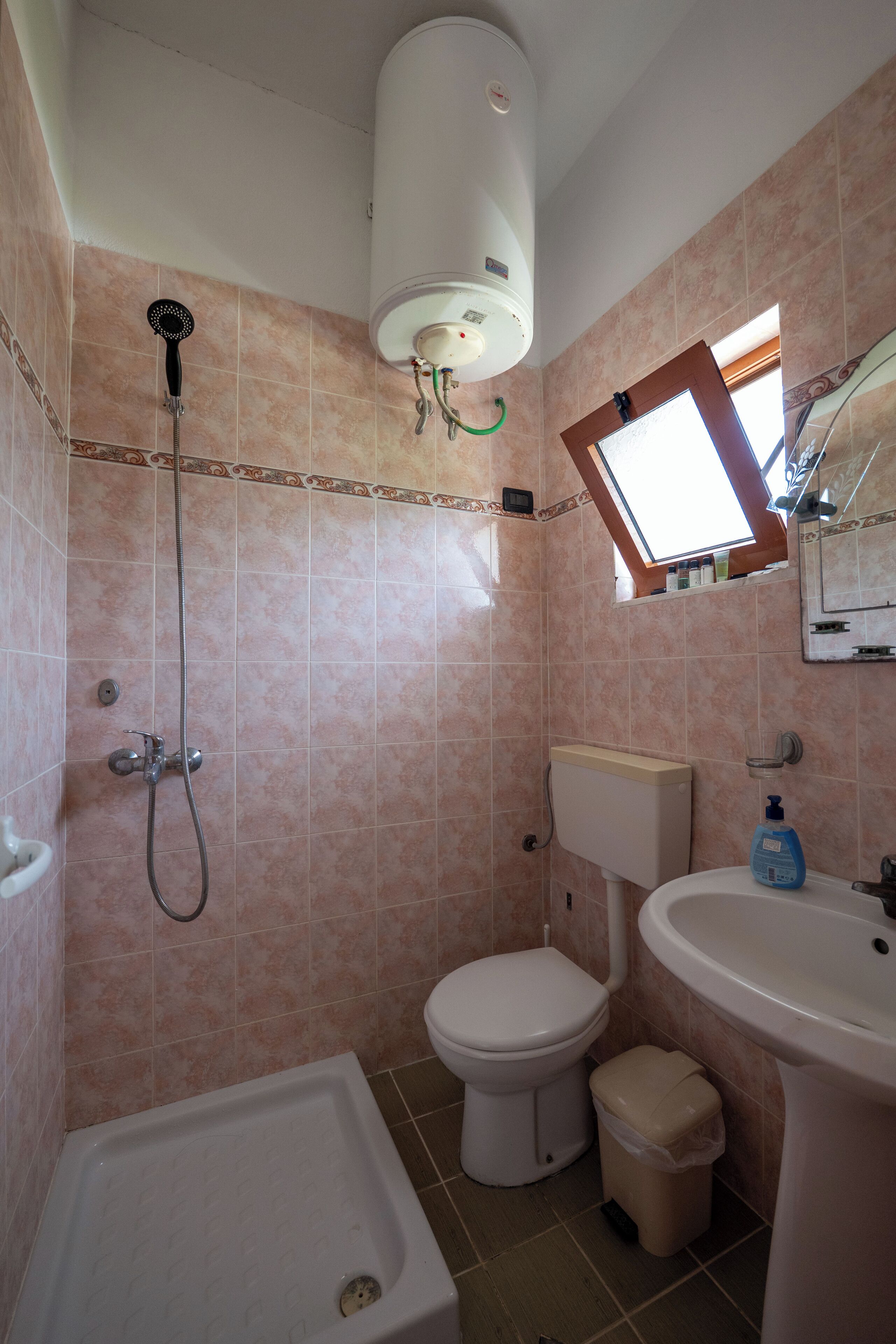 Bagno con doccia, WC e lavandino, con piastrelle rosa e una finestra.