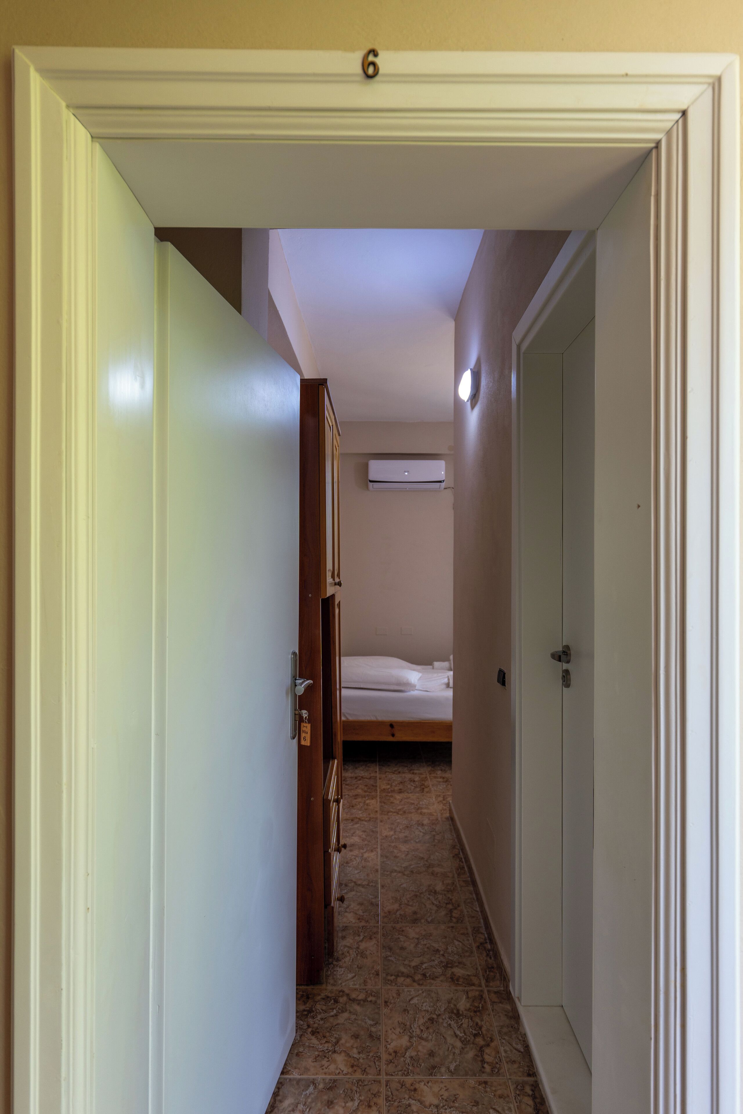 A narrow hallway leading to a bedroom with a bed and an air conditioning unit on the wall.