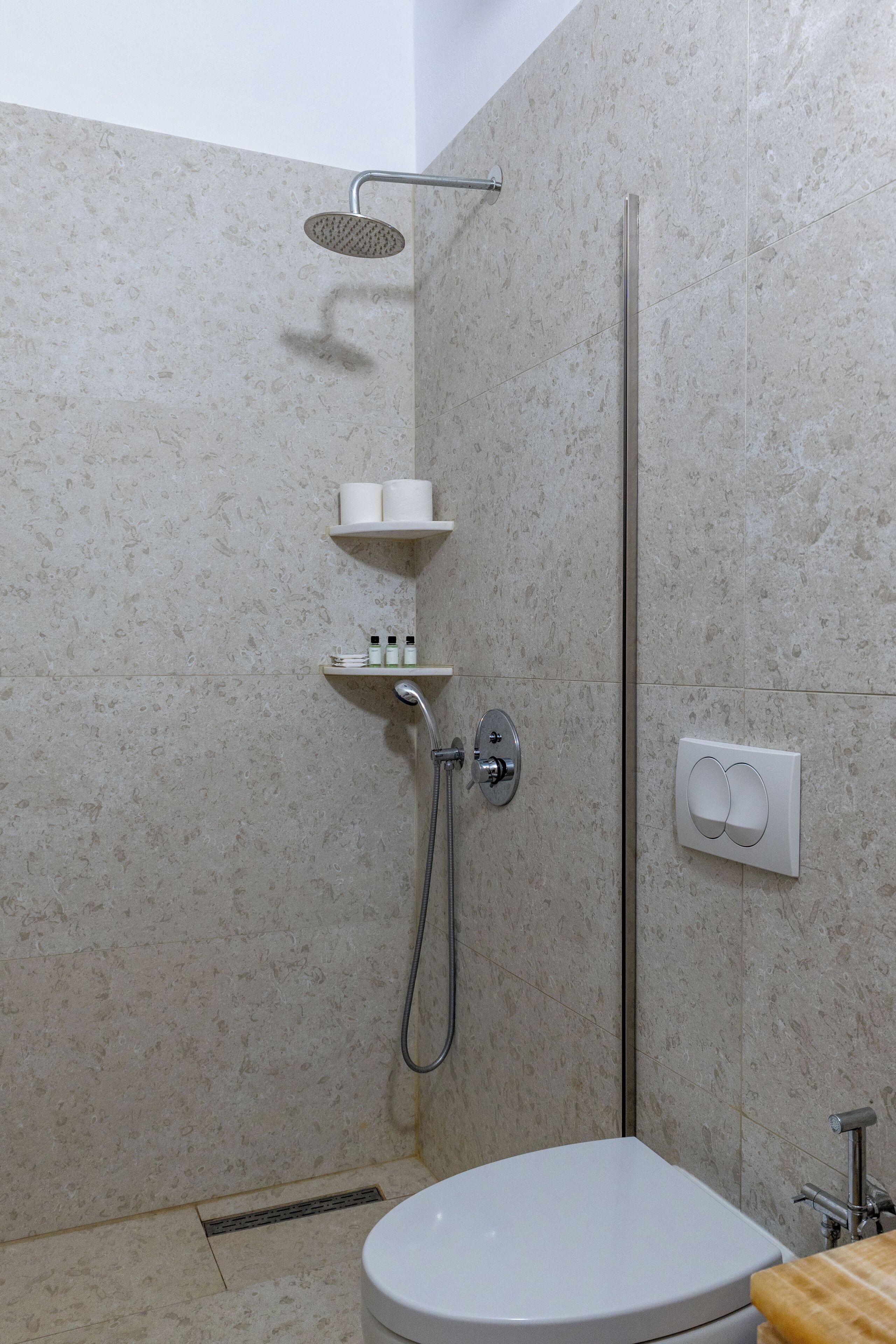 Een moderne badkamer met een douche, toilet en een plank met toiletartikelen.