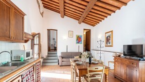 A spacious kitchen with wooden cabinets, a dining area with a table and chairs, a sofa, and a television on a wooden cabinet. - Exclusive Resort, Pool & Waterfall - A12 (Loro Ciuffenna)