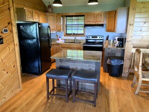 A kitchen with wooden cabinets, a black refrigerator, a stove, and two bar stools. - Breathtaking Views!  Spacious Cabin, HotTub, pool table near PF & Gatlinburg ⛰️ (Sevierville)