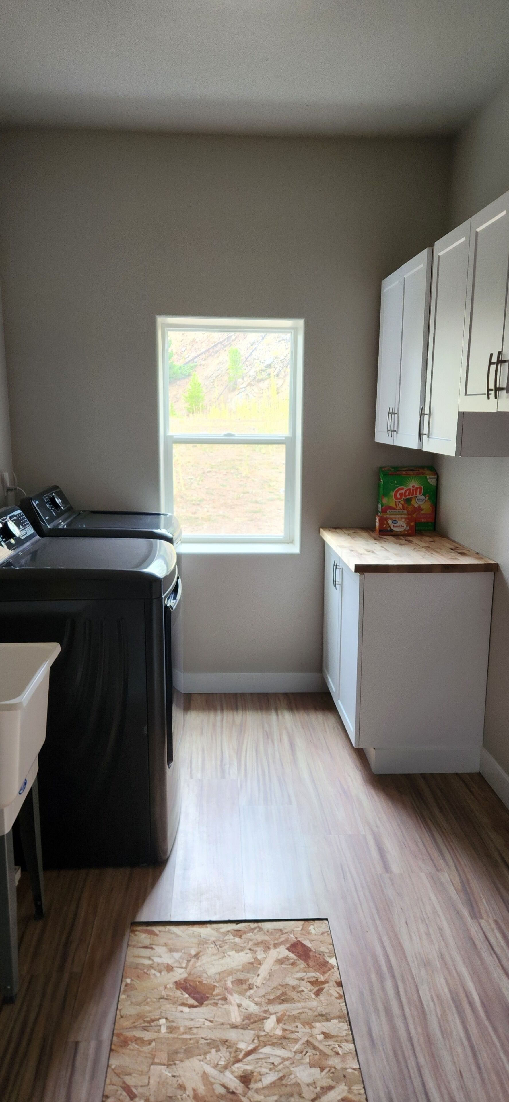 A compact kitchen with a washer and dryer, a small countertop, and a window with a view of trees.