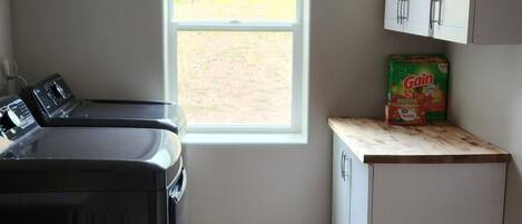A compact kitchen with a washer and dryer, a small countertop, and a window with a view of trees.