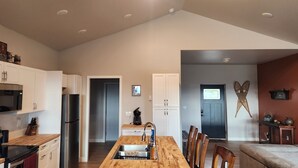 Una cocina moderna con armarios blancos, un refrigerador de acero inoxidable, un microondas y una mesa de comedor de madera.