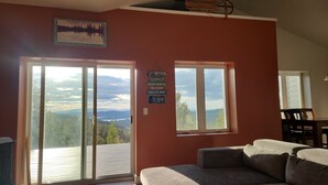 Un salón con sofá, una mesa de comedor y dos ventanas que ofrecen vistas a un bosque y montañas.