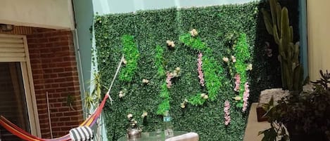 Eine Außenpatio mit grüner Wand, zwei Stühlen, einem Tisch und einer Hängematte.
