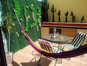 A hammock chair set up on a patio with a green wall backdrop, a round table with chairs, and a row of cacti on a shelf. - Beautiful And Comfortable Near To Subway (Buenos Aires)