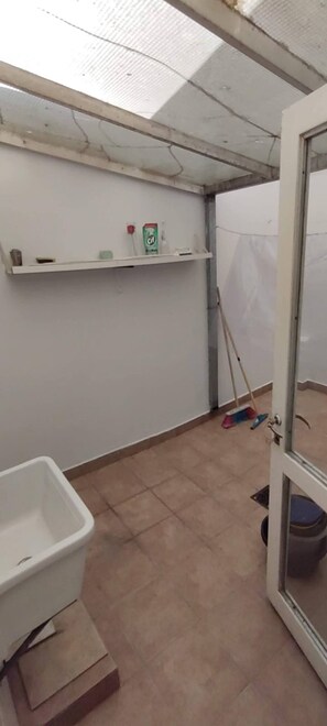 A room with a white bathtub, a broom, and a mop leaning against the wall. - Beautiful And Comfortable Near To Subway (Buenos Aires)