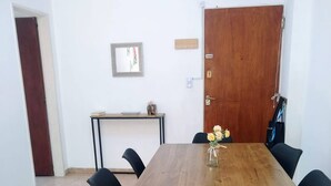 A dining area with a wooden table and black chairs, a small side table with a bowl and a decorative item, and a door with a wooden panel.