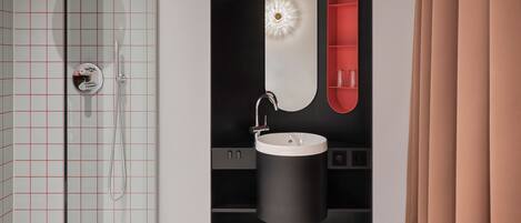 A modern bathroom with a glass shower enclosure, a black sink with a round mirror, and a red shelf.