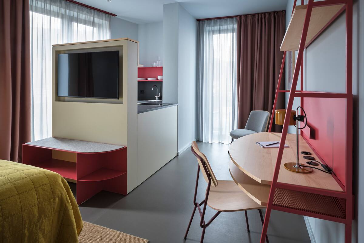Ein kompaktes Hotelzimmer mit Küchenzeile, einer kleinen Essecke, einem Bett und einem Fernseher.