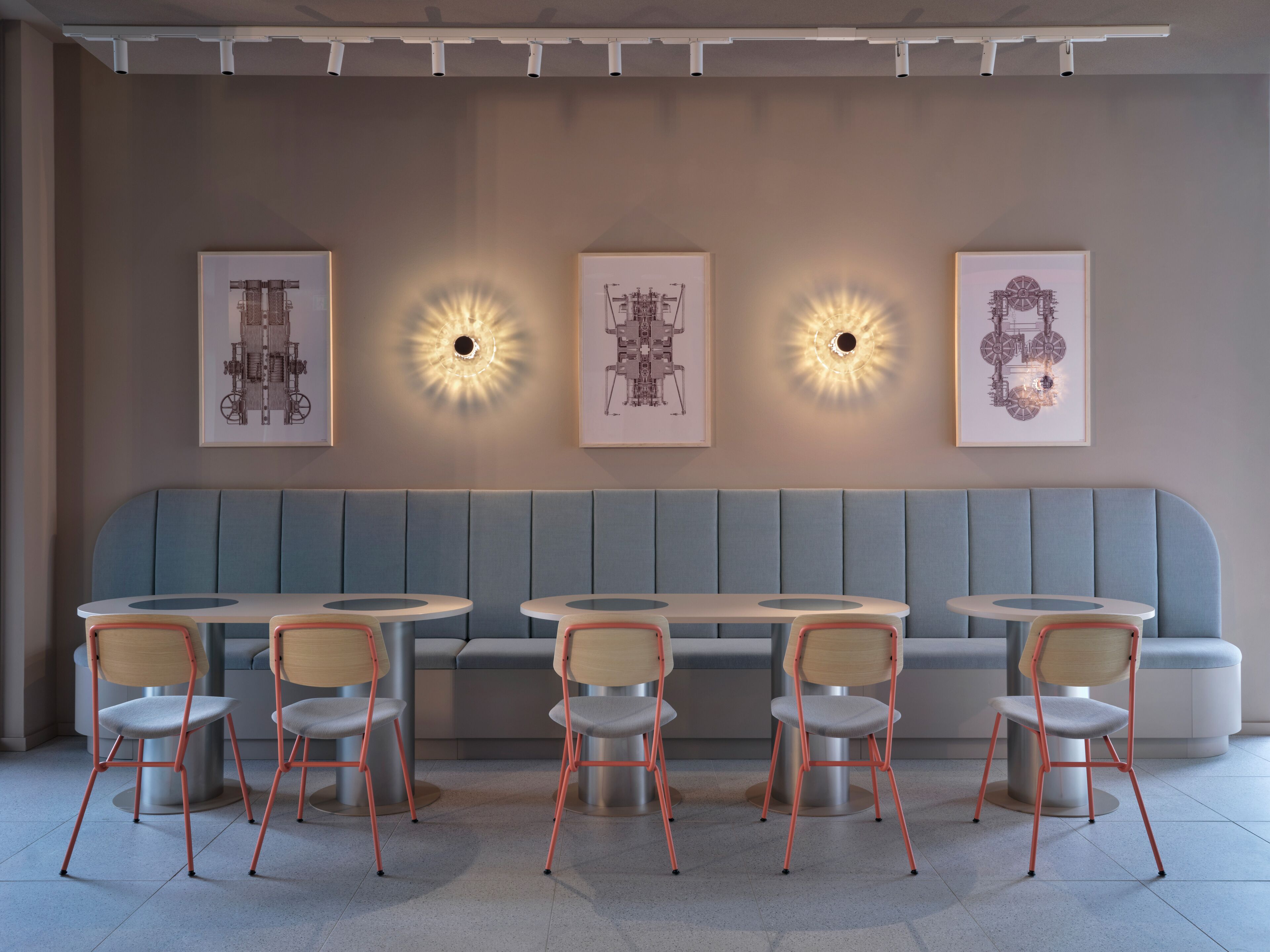 Un interior de restaurante moderno con una zona de asientos en cabinas azules, mesas redondas y sillas.