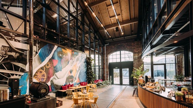 A spacious cafe with high ceilings, exposed brick walls, and large windows. - Noxx Hotel (Marburg)