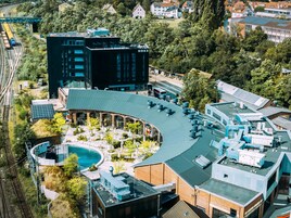 Un hotel moderno con techo curvo, piscina al aire libre y una vía de tren cerca.