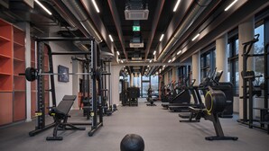 A gym with various exercise equipment, including treadmills and weight machines, and a large window providing natural light. - Noxx Hotel (Marburg)