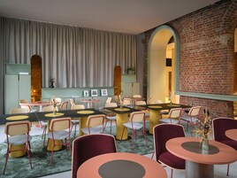 Un comedor moderno con mesas y sillas redondas, una pared de ladrillo y un ventanal con cortinas.