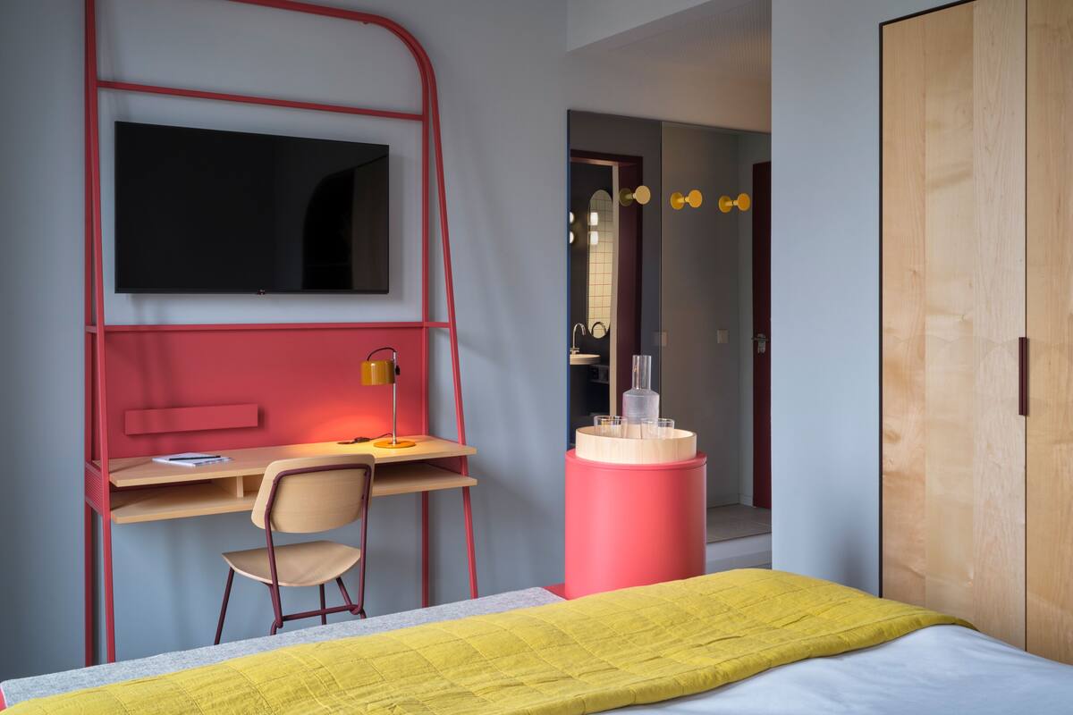 Ein Schlafzimmer mit Bett, Schreibtisch, Stuhl, Fernseher, Spiegel und Kleiderschrank.