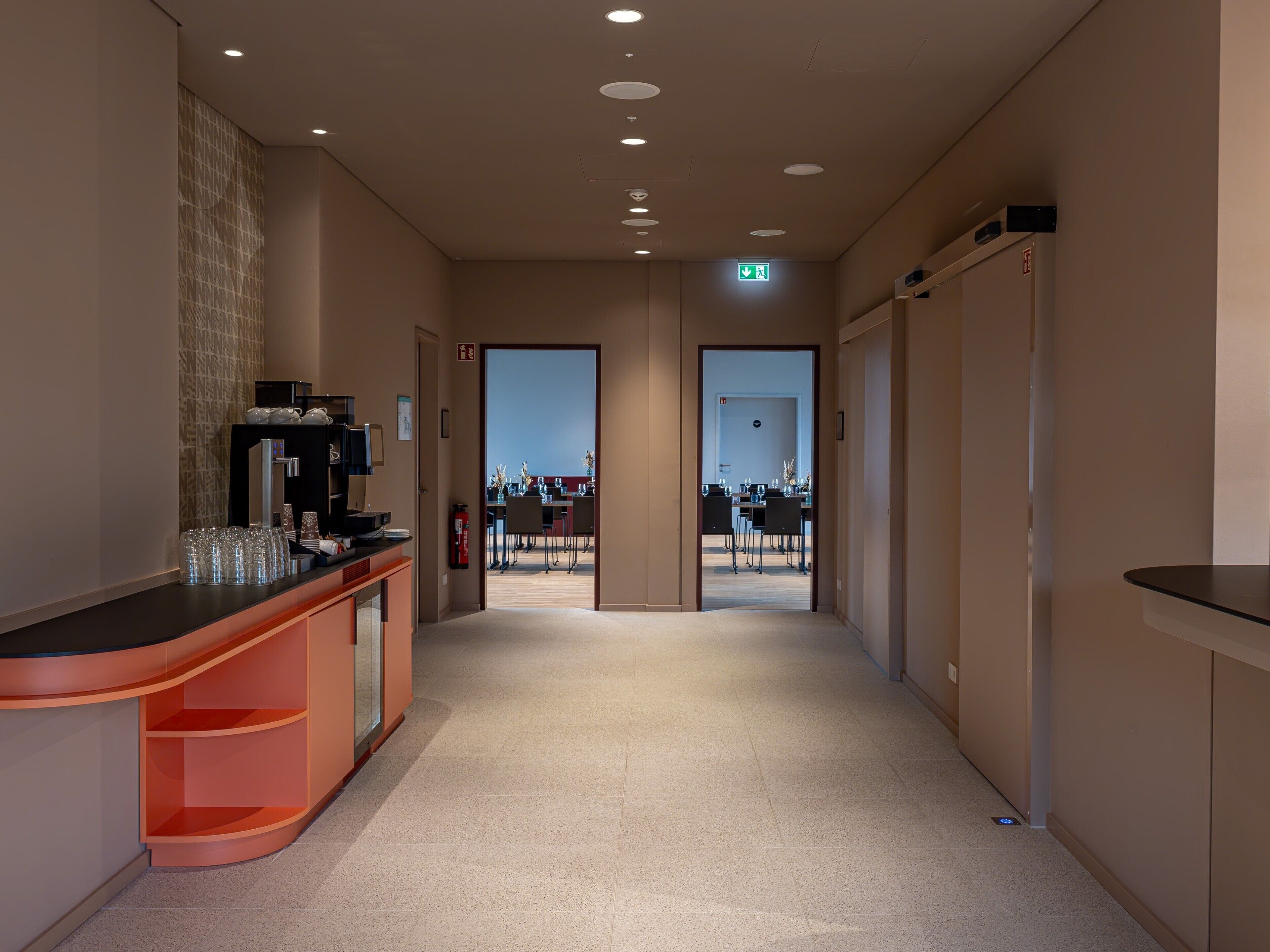 A hotel corridor with a reception desk, a fire extinguisher, and an exit door.