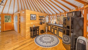 A yurt interior with wooden walls, a kitchen area with a refrigerator, stove, and microwave, and a patterned rug on the floor. - Unique authentic yurt stay near Yosemite National Park  (Wishon)