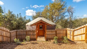 A wooden cabin with a pitched roof, surrounded by a wooden fence, set in a wooded area. - Unique authentic yurt stay near Yosemite National Park  (Wishon)