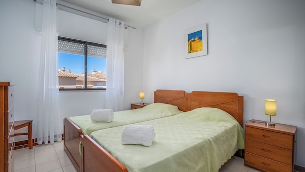 Ein Hotelzimmer mit zwei Betten, einem Fenster mit Blick auf Gebäude, einem Bild an der Wand und einem Nachttisch mit Lampe.