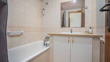 Un baño con bañera, lavabo con espejo y ducha.