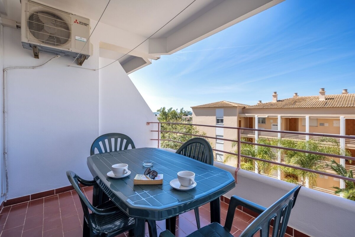 A balcony with a table and chairs, a white cup, a book, and a pair of sunglasses.
