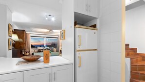 A kitchen with white cabinets, a wooden bowl on the counter, and a white refrigerator with gold handles.