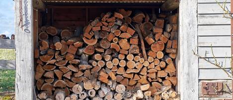 Un cobertizo de madera con techo de metal corrugado, lleno de leña apilada ordenadamente.
