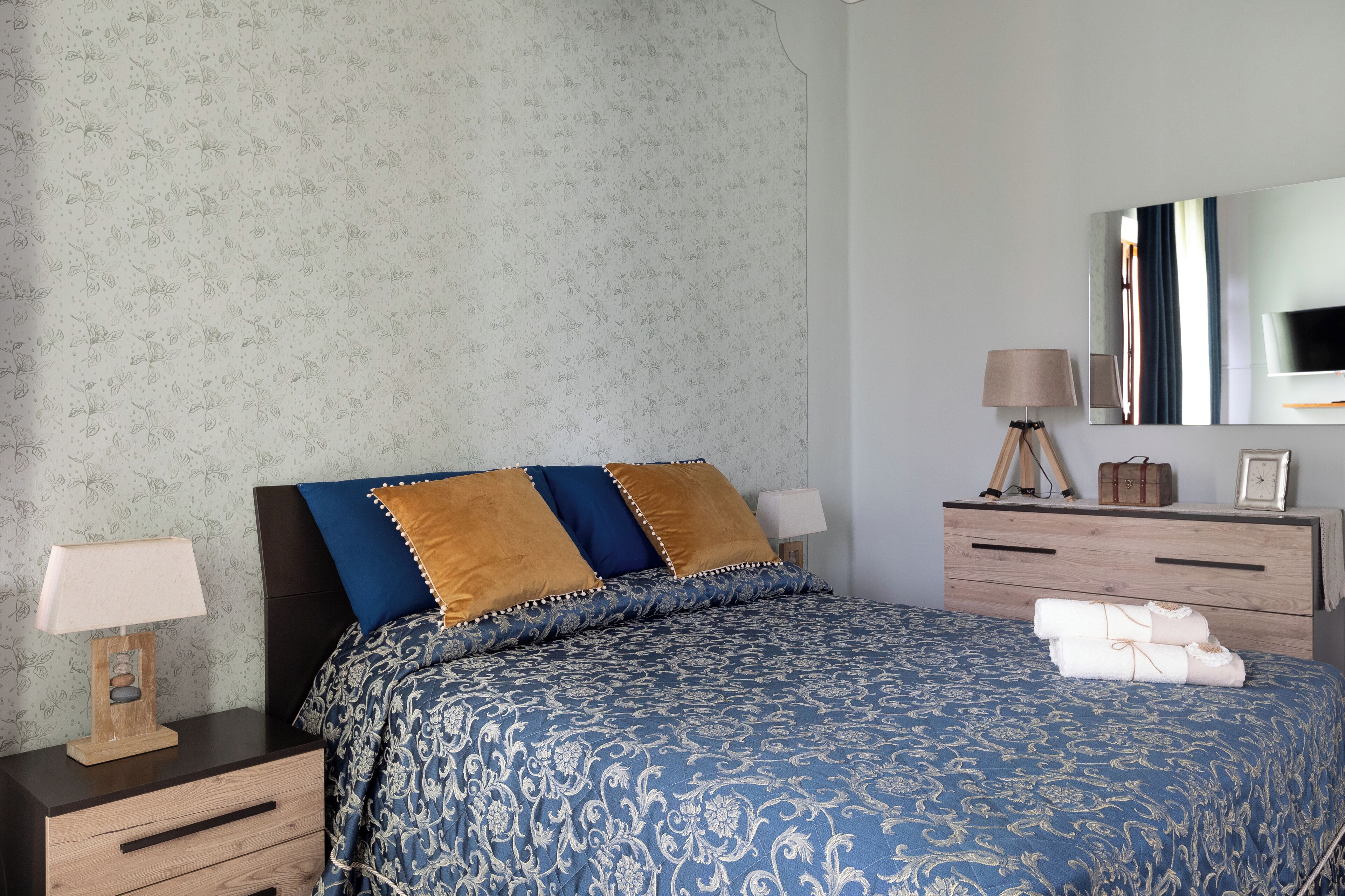Ein Schlafzimmer mit Bett, Nachttischen, einer Kommode und einem Spiegel.