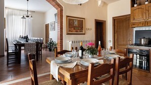 A dining area with a wooden table set for six, a kitchen with wooden cabinets, and a dining area with a brick archway. - "A CASA DI FRANCA" PRIVATE VILLA IN CHIANTI
A RURAL REFUGE FOR FAMILIES (Gambassi Terme)