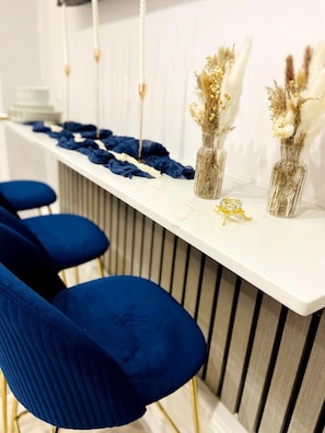 A bar area with a white countertop, blue chairs, and decorative vases with dried flowers. - Inviting 3-bed Apartment in London (London)