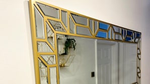 A rectangular mirror with a geometric gold frame mounted on a plain white wall.