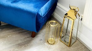 A bed with a blue velvet cover, a gold and glass lantern, and a wooden floor.