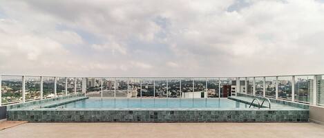 A rooftop infinity pool with a city view, surrounded by a glass railing.