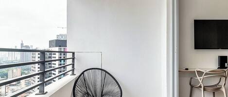 A balcony with a black chair, a desk with a computer, and a TV on the wall.