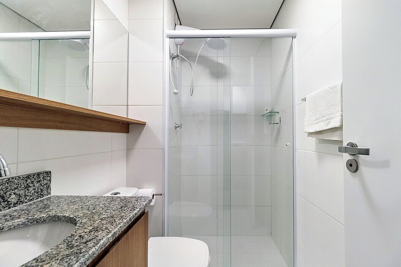 Un bagno moderno con box doccia in vetro, piano di lavoro in granito e un water bianco.