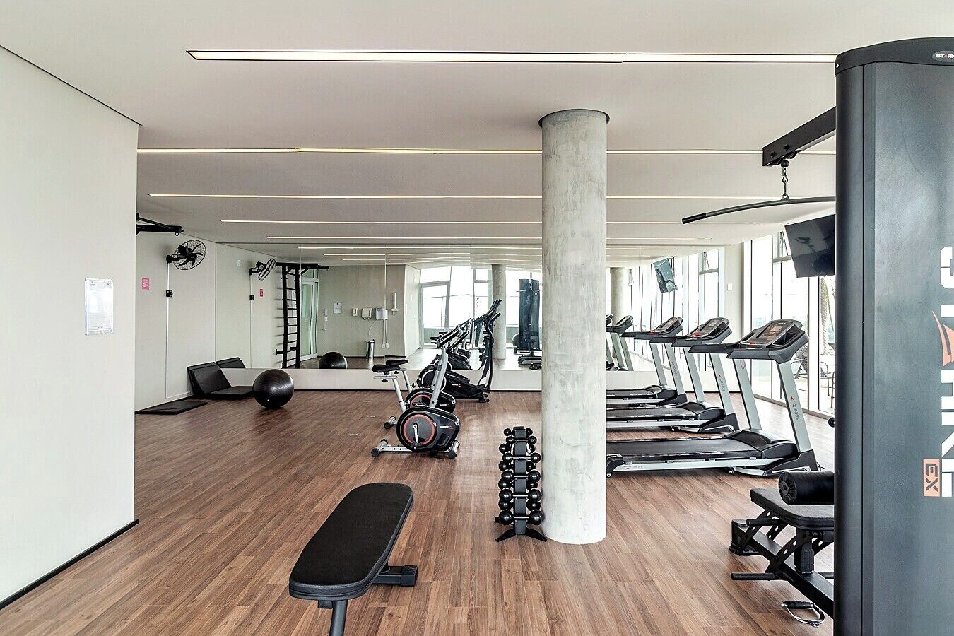 Et moderne fitnesscenter med træningsudstyr, store vinduer og trægulv.
